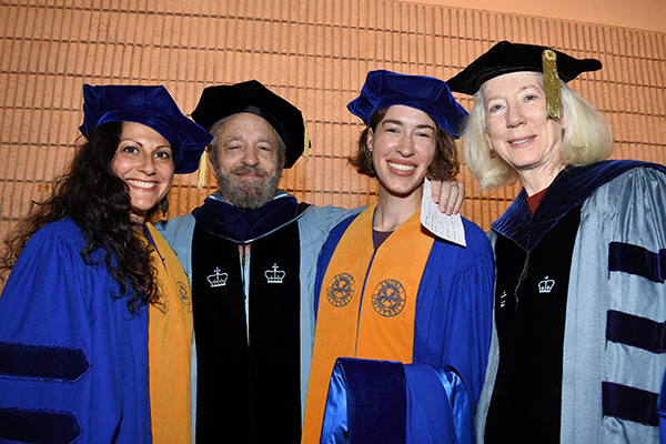 Two female graduates pose happily in their regalia with their male and female faculty mentors.